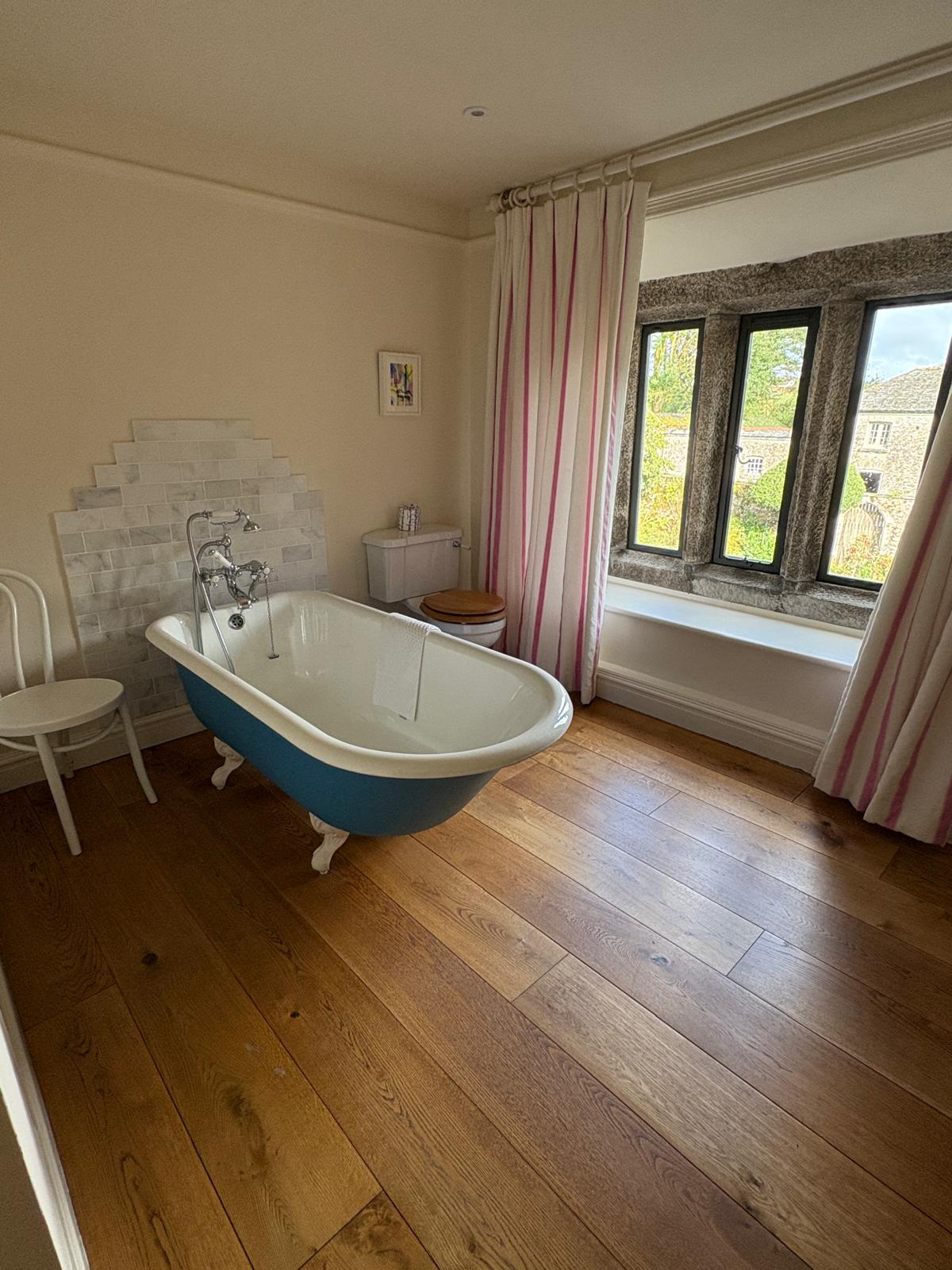 Blue roll-top bath in a country bathroom with wooden floors