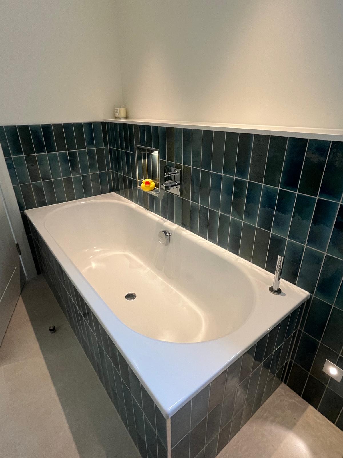 Deep bath with teal tiles and a lit shelf niche
